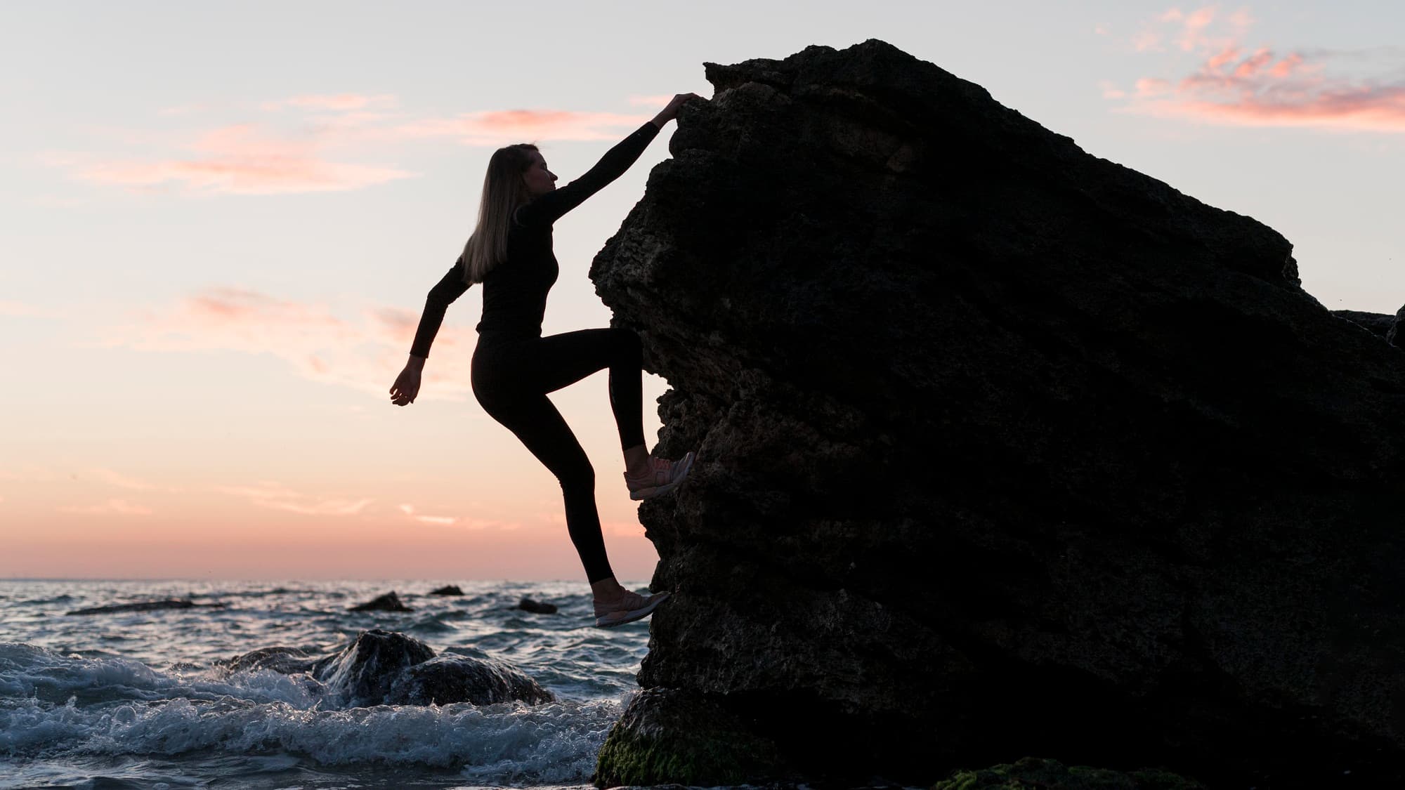 long shot woman climbing a rock next to the ocean